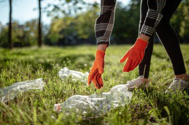 Kadın yeşil çimenlikteki plastik şişeleri topluyor. Güneşli bir günde bir gönüllü parkı temizler. Temizlik, kirlilik, ekoloji ve plastik konsept