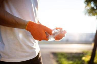 Eldiven takan bir adam elinde kullanılmış bir plastik şişe tutuyor. Güneşli bir günde bir gönüllü parkı temizler. Temizlik, kirlilik, ekoloji ve plastik konsept