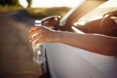 Kadının eli arabanın camından plastik bir şişe fırlatıyor. Şoför kullanılmış su şişesini yola attı. Çevre ve çöp konseptinin sorumsuz kirliliği
