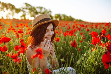 Genç bir kadın kırmızı haşhaş tarlasının ortasında oturur ve çiçekleri koklar. Kız çiçeklerin arasında güneşli bir günün tadını çıkarıyor. Bahar ve gün batımı kavramı