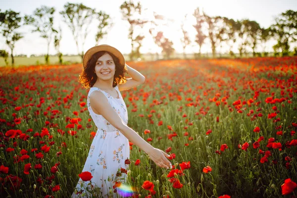 Young woman having fun in the middle of the red poppy field at spring. Girl wearing white light dress enjoys freedom and good weather. Spring and joy concept