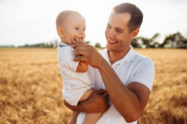 Bir baba oğlunu altın buğday tarlasının ortasında ellerinin arasında tutar. Güneşli bir günde çocuğuyla dışarıda eğlenen bir adam. Aile değerleri ve mutluluk kavramı