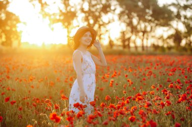 Mutlu kız haşhaş tarlasında duruyor. Çiçeklerle gün batımında esmer. Batan güneşin arka planına karşı şapkalı ve beyaz elbiseli bir kadın. Kız elini çiçeklerin üzerinden geçiriyor.