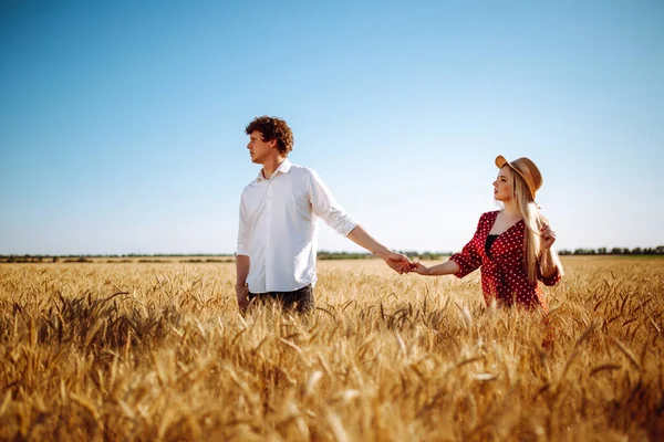 快乐的男女正在麦田里日落时散步 一对恋人在日落时牵着手 一个穿着圆圆点连衣裙的女孩和一个穿白衬衫的男人 — 图库照片