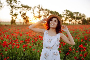 Güzel bir kız gün batımında gelincik tarlasında yürüyor. Güzel bir yaz bahçesinde hasır şapkalı genç bir kadın. Yumuşak günbatımı ışığı. Güzel bir tarlada esmer bir kızın portresi.