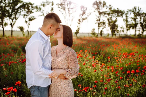 浪漫的年轻夫妇拥抱在红色美丽的罂粟地里 爱的男孩和女孩站在一起 拥抱和亲吻 表达彼此的感情 家庭和爱情概念 — 图库照片