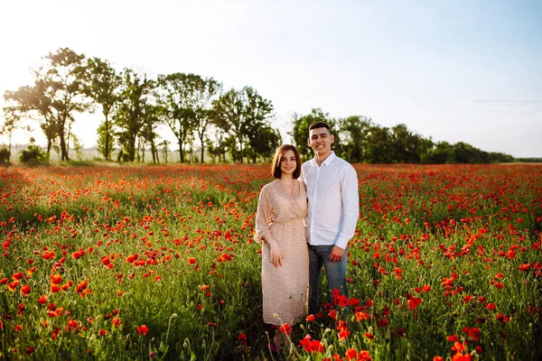 在一个阳光灿烂的日子里 一对浪漫的年轻夫妇站在红色的罂粟地里 彼此示爱 快乐的男孩和女孩喜欢在红花间共度时光 热爱和平与家庭价值观 — 图库照片