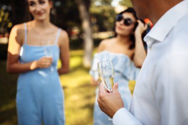 Elinde bir bardak şampanyayla bir kutlama şirketinin arka planında duran bir adam. Düğün, doğum günü, yıldönümü. Düğünde şampanya içen bir grup insan.