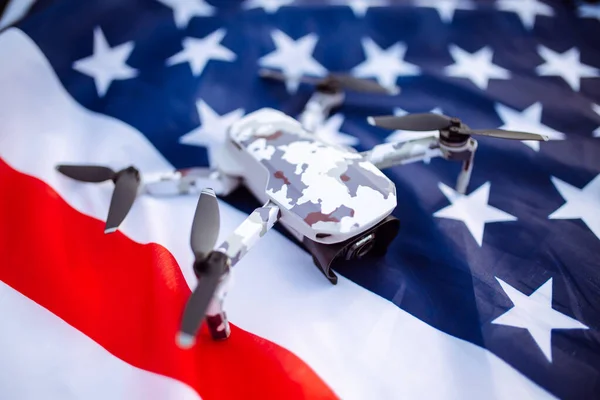 A closeup shot of a lying drone. The drone lies on the American flag against the background of a green field of wheat. Independence Day. 4th of July. Technologies, innovation