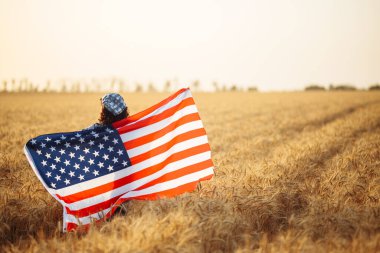 Genç bir kadın elinde Amerikan bayrağıyla buğday tarlasının ortasında duruyor. Özgürlük kavramı. Bağımsızlık Günü. 4 Temmuz