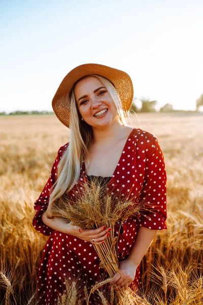 Portrait of young beautiful girl in wheat field. Happy blonde woman in straw hat and dress with peas in the middle of a field with a wheat computer in her hands. Summer landscape, sunset, soft colors