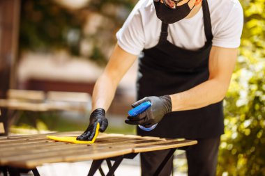 Koruyucu maske takmış bir garson ve eldivenlerle dezenfektanla masayı temizler ve hoş karşılanan müşteriden önce silerdi. Pandemik sağlık riski, koronavirüs