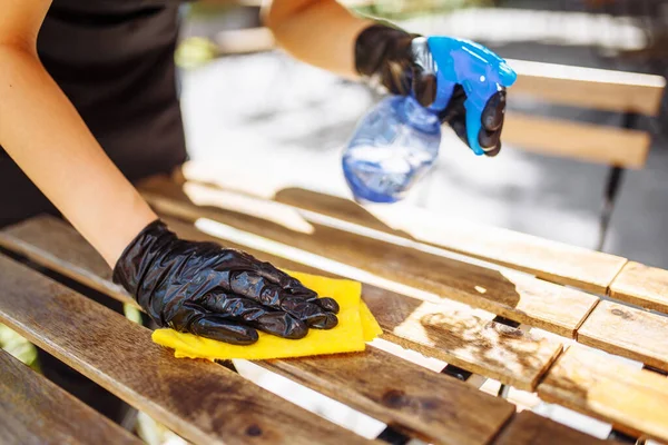 Bir garsonun eldiven ve koruyucu maskeyle bir kafe ya da restoran açılmadan önce mobilyaları dezenfekte ederken yakın plan fotoğrafı.