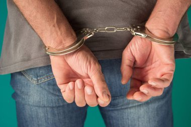 Elleri arkadan kelepçeli tutuklu bir adam. Kelepçeli kot pantolonlu adamın yeşil, insan hakları kavramında tek başına durması.