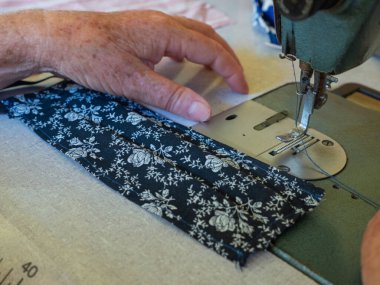 Dikiş makinesiyle çalışan olgun bir kadın Corona virüsünün yayılmasını önlemek ve önlemek için ev yapımı tıbbi maske takıyor.