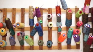 Çok renkli iplik makaraları ahşap bir stantta asılı.