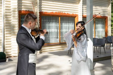 Kemancıların ikilisi. Paltolu bir adam ve gece elbiseli bir kadın keman çalıyor..