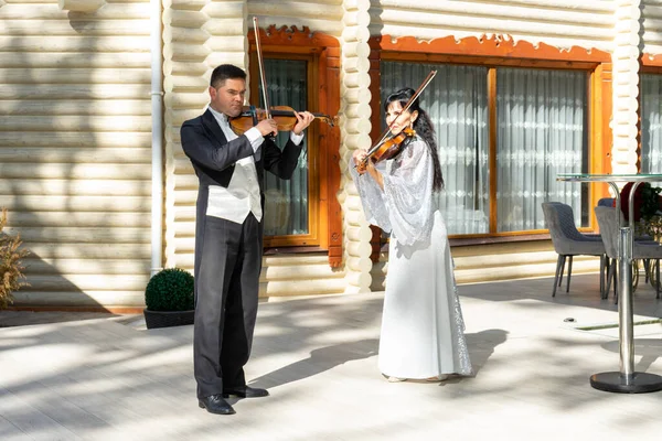 Duo of violinists. A man in a tailcoat and a woman in an evening dress play the violin.