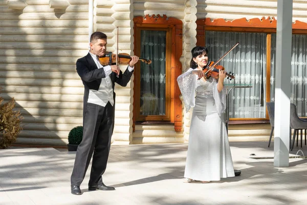 Duo of violinists. A man in a tailcoat and a woman in an evening dress play the violin.