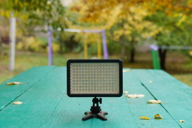 Serene parkındaki yeşil bir masaya bir ışık paneli konur. Renkli sonbahar yaprakları zemini kaplıyor ve ağaçlar huzurlu bir zemin oluşturuyor..