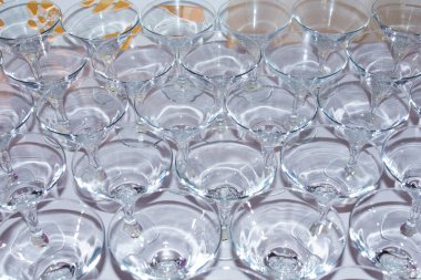 Çoklu berrak cam bardaklar bir masanın üzerinde simetrik bir şekilde düzenlenir, bir olaya ya da kutlamaya hazırdırlar..