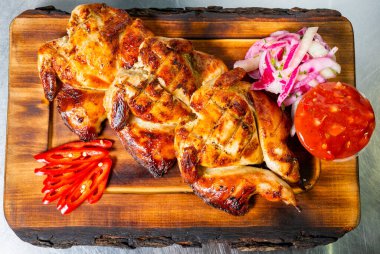 Sulu ızgara tavuk parçaları ahşap bir tabakta, yanında da salsa, soğan ve kırmızı biber..