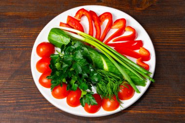 Domates, salatalık ve dolma biber de dahil olmak üzere renkli sebzeler, sanatsal olarak beyaz bir tabakta pişirilmeye hazırdır..