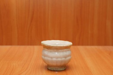 Bu seramik fincan, sıcak içecekler servis etmek için mükemmel, pürüzsüz bir ahşap masanın üzerinde duruyor. Basit tasarımı zarif işçiliğini vurguluyor..