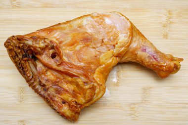 Lezzetli bir tütsülenmiş tavuk bacağı ahşap bir kesme tahtasının üzerinde duruyor, zengin rengini ve dokusunu sergiliyor. Yemekler ve toplantılar için mükemmel..