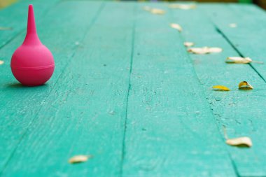 Parlak pembe bir ampul sarı yapraklarla dağılmış yeşil bir ahşap masada oturur. Sahne canlı bir sonbahar atmosferini yakalıyor..