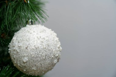 Beyaz malzemeden yapılmış bir top bir çam dalına asılıyor. Bayram atmosferi için bir dekorasyon..