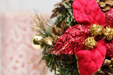 Çiçekler ve çam kozalaklarından yapılan kırmızı ve altın tatil süslerinin yakın görüntüsü. Sahne, sezon boyunca şenlik ruhunu gösteriyor..