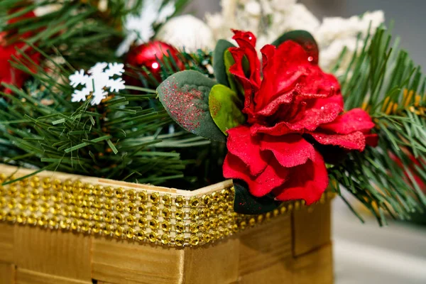 Tatil dekorasyonunda kırmızı çiçekler, yeşil yapraklar ve parlak süsler olan bir sepet görülüyor. Sahne şenlikli bir atmosferi yakalıyor..