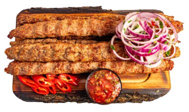 Izgara kebaplar ahşap bir tahtanın üzerinde kırmızı biber dilimleri, soğan halkaları ve bir kase salsa sosuyla sergilenir..