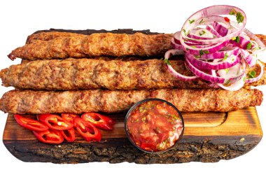 Izgara et şişleri, yanında küçük bir kase sos ve dilimlenmiş sebzelerle ahşap bir tahtaya konur..