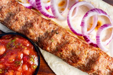 Dilimlenmiş soğan ve bir kase salsa sosuyla birlikte ekmek üzerine yerleştirilmiş ızgara et şişi..