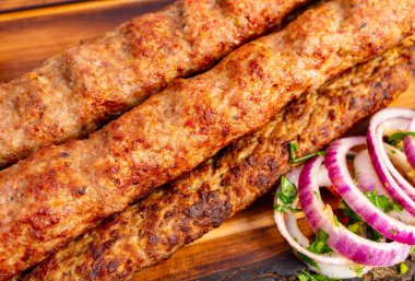 Üç sulu kebap, tahtanın üzerinde soğan ve taze otların yanında, toplanmaya hazır bekliyor..