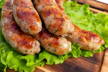 Sosisler ızgara yapılır ve taze marulun üzerine konur, servis edilmeye hazırdır. Yemekler ahşap bir yüzeye düzgün yerleştirilmiş..