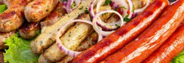 Izgara sosisler, soğan ve taze yeşilliklerle servis tabağına konur. Yemek ya da yemek için hazır görünüyor..