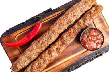 İki uzun ızgara kebap, ahşap bir tahtaya kırmızı biber ve bir kase salsa sosunun yanına konur..