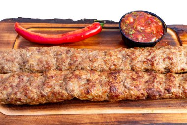 İki uzun kebap, bir kase salsa ve kırmızı biberin yanında tahtadan bir tahtaya dizilir..