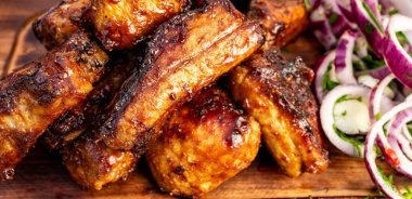 Sulu barbekü kaburgaları ahşap bir tahtada dilimlenmiş soğan ve biberli salatanın yanında istiflenir. Yemekler mangal için hazırlandı..