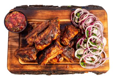 Bir tabakta dilimlenmiş soğan ve bir kase soslu salatalığın yanında ızgara tavuk kanadı var..