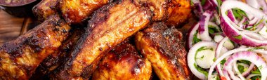 Pişmiş tavuk kanatları ahşap bir tahtaya konur. Yanında taze soğanlı salata ve sosla birlikte..