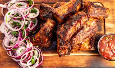 Izgara pirzola, dilimlenmiş soğan, otlar ve küçük bir kase salsa sosunun yanında ahşap bir tabakta dinleniyor..