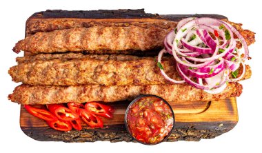 Kebaplar dilimlenmiş soğanlar, domatesler ve küçük bir kase sosla ahşap bir tahtada düzenlenir. Bu yemek lezzetli görünüyor..