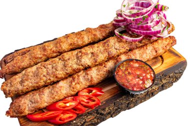 Tahta bir tahtaya üç uzun kebap yerleştirilir. Kırmızı soğan ve dilimlenmiş biber bir kase sosun yanında düzenlenir..