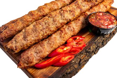 Izgara et şişleri, dilimlenmiş domatesler ve küçük bir kase sosla birlikte ahşap bir tahtanın üzerinde oturur. Bu yemek servis edilmeye hazır..