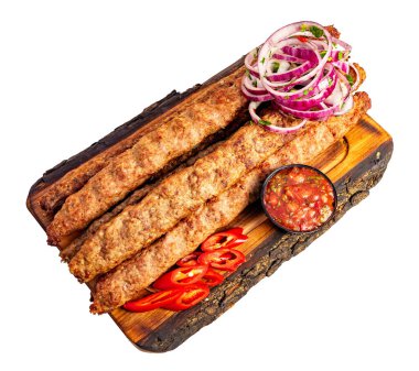 Tahta bir tahtaya üç uzun kebap yerleştirilir. Üzerine soğan ve kırmızı biber dilimleri oturur. Yakınlarda küçük bir kase sos var..