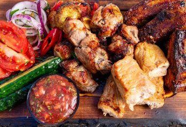 İnsanlar yaz etkinlikleri sırasında ahşap tabakta servis edilen çeşitli ızgara et ve taze sebzelerden hoşlanırlar..